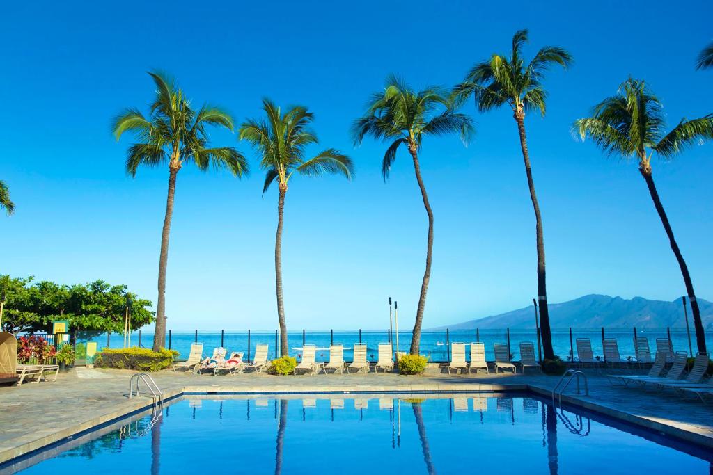 a pool with palm trees and the ocean in the background at AEI at Kaanapali Shores in Lahaina