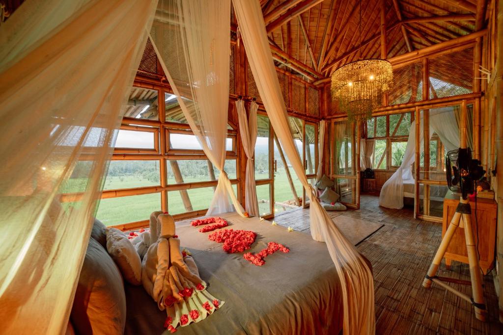 una camera da letto con un letto a baldacchino con fiori rossi di Sidemen Luxury Nyan Bali - Bamboo House a Selat