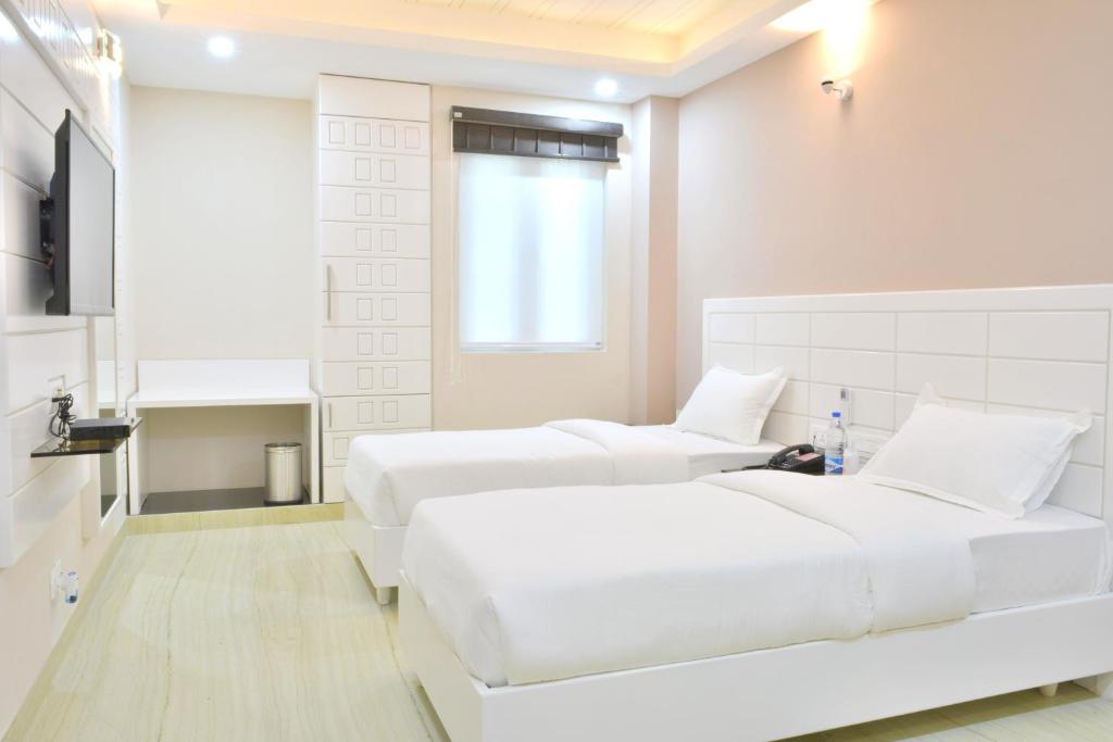 um quarto branco com 2 camas e uma televisão em Hotel Tara Palace Redfort em Nova Deli