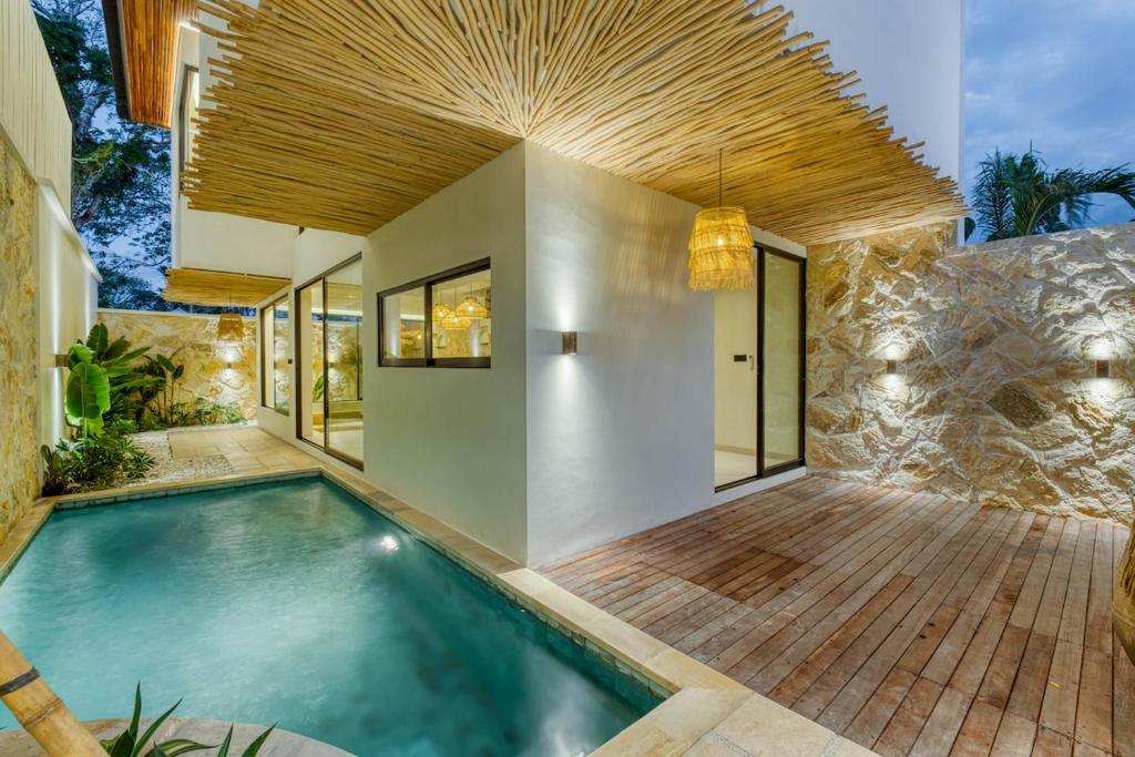 Anjuna Surf & Sunset 2BR Villas in Uluwatu في أُلُواتو: حمام سباحة داخلي مع سطح خشبي بجوار منزل