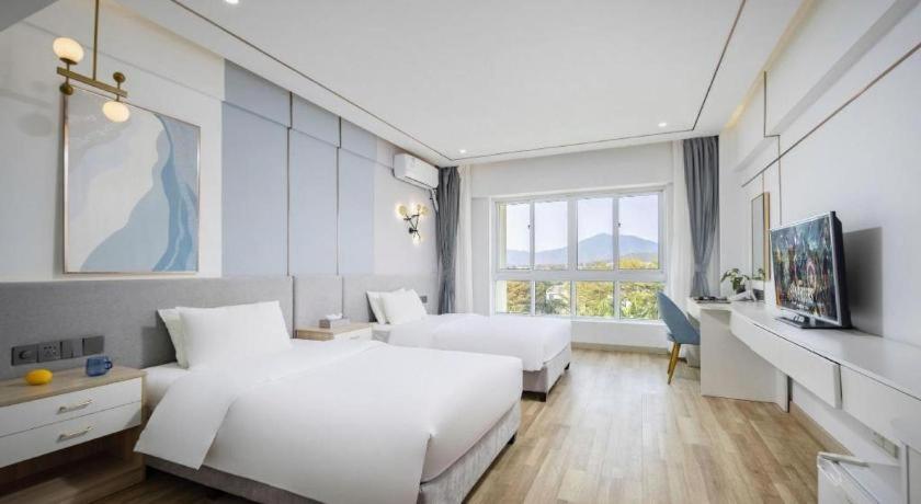 a white bedroom with two beds and a window at Sanya Summer Beach Sea View Hotel in Sanya