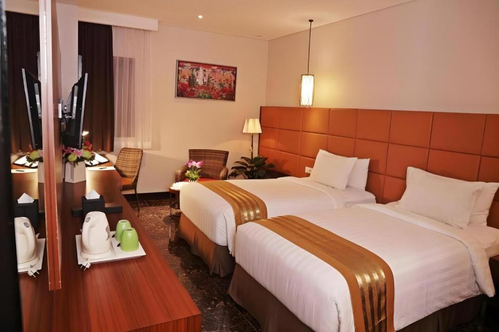 a hotel room with two beds and a desk at Atrium Premiere Cilacap in Cilacap