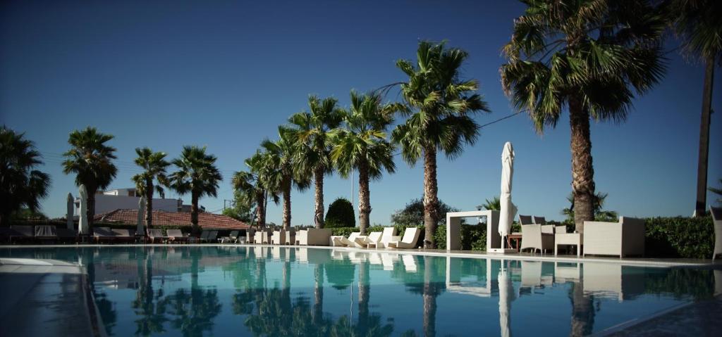 ヴォロスにあるValis Resort Hotelのヤシの木と白い椅子が備わるスイミングプール