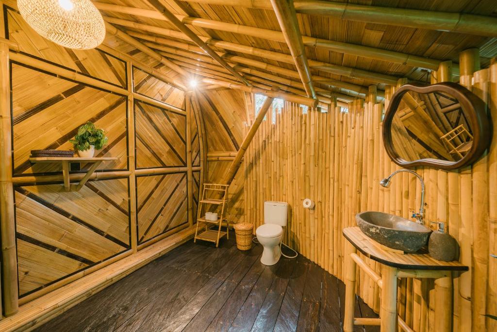 a bathroom with a sink and a toilet in a wooden room at Nirvana Bamboo House by Arcada Bali in Selat