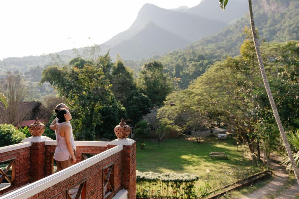 a woman standing on a balcony looking at the mountains at Ashi Guesthouse Chiangdao in Chiang Dao