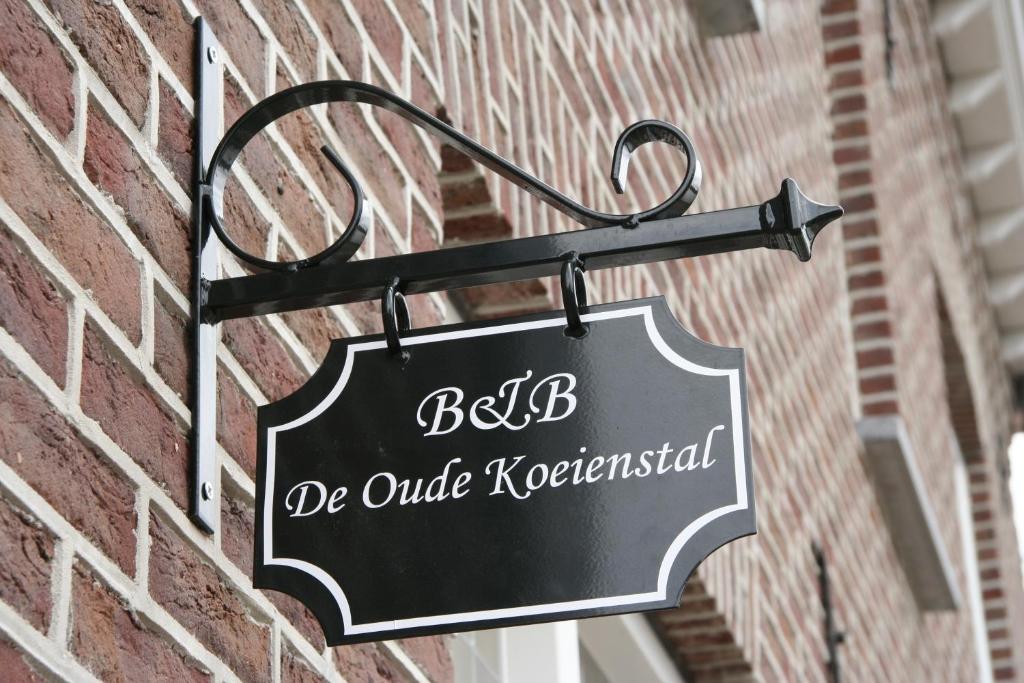 um sinal preto pendurado no lado de um edifício de tijolos em De Oude Koeienstal em Schimmert