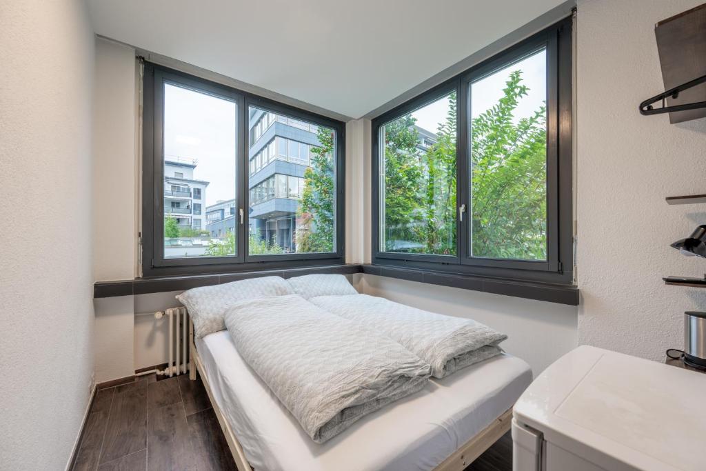 a bed in a room with three windows at Mount Pilatus Rooms Lucerne in Luzern