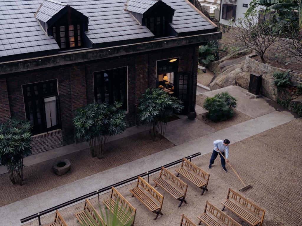 a man is mowing chairs in front of a building at Gulangyu HUMBLE HALL Resort Hotel - Century-Old Historic Building & Banyan Courtyard - Near Sunlight Rock - Free Handmade Afternoon Tea & Breakfast - Pier Luggage Service - Free Island Walking guide & Hidden Route Guide - Paid English Tour Guide Service in Xiamen
