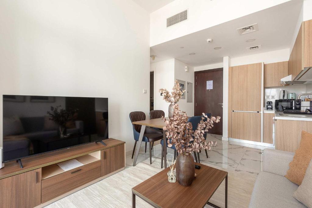 Una sala de estar con un televisor y una mesa con sillas. en Silkhaus Deluxe 1BR in Masdar City at Oasis, en Abu Dhabi Intl