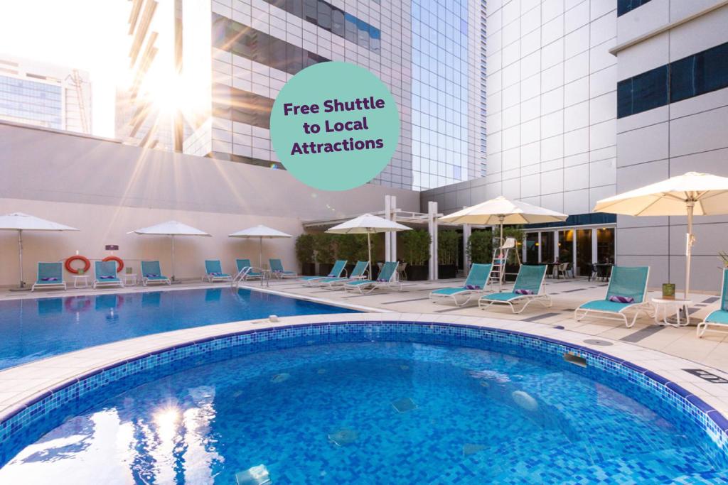une piscine dans un hôtel avec un panneau indiquant une navette gratuite vers les attractions locales dans l'établissement Premier Inn Abu Dhabi Capital Centre, à Abu Dhabi
