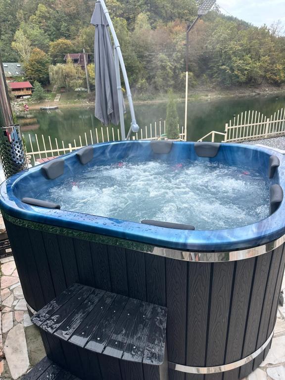 Una bañera de hidromasaje con sombrilla junto a un lago. en Leo Green House, en Moara Ungurului