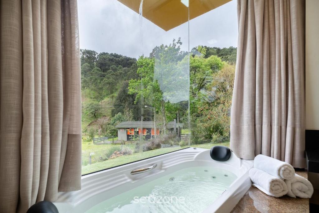 a bath tub in a room with a large window at Casa c/ Lareira e Banheira em Urubici CLA0000 in Urubici