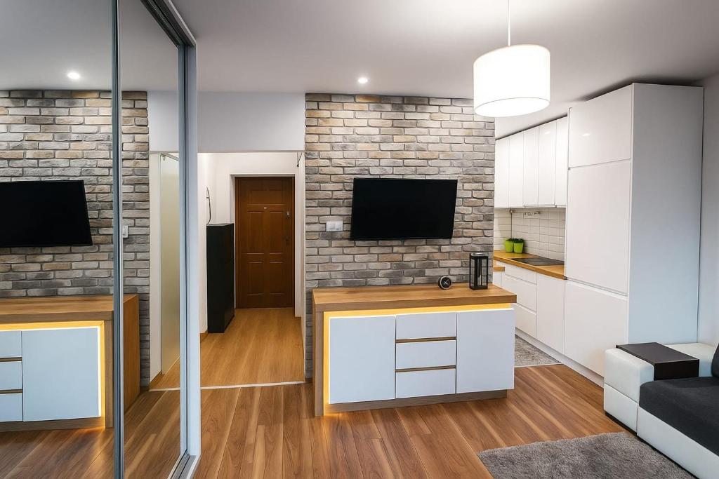 a kitchen with white cabinets and a tv on a brick wall at Śliczny Apartament obok Manufaktury na wyłączność, parter, blok, in Łódź
