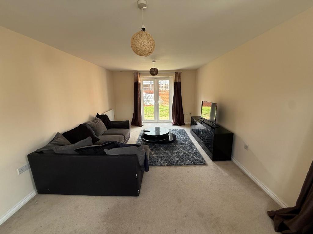 ein Wohnzimmer mit einer schwarzen Couch und einem Fernseher in der Unterkunft Charming Aylesbury Retreat with 4 Bedrooms in Weedon