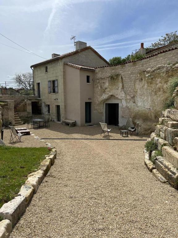 a stone building with chairs and a house at Le troglo du château in Beaumont