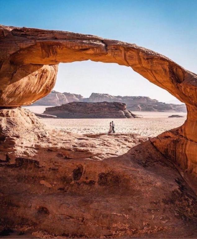 Una persona parada en el desierto debajo de un arco en el desierto. en Bedouin Luxe Camp & Tour, en Wadi Rum