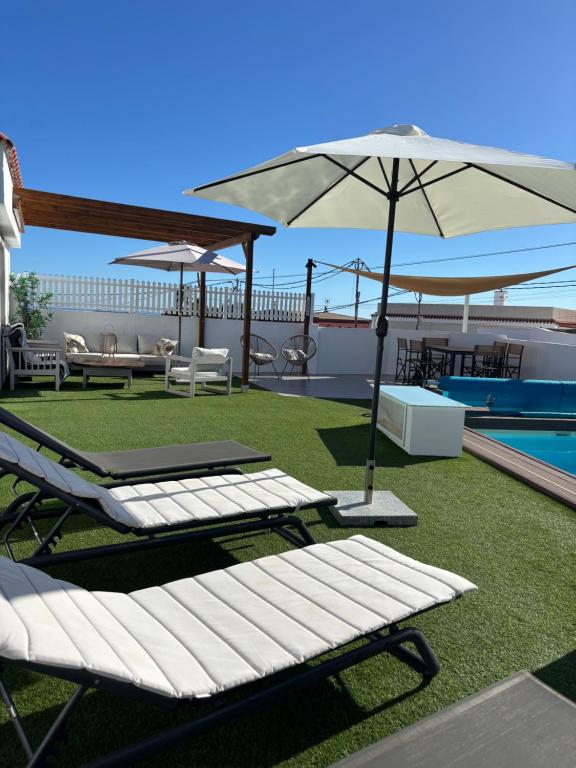a patio with lounge chairs and an umbrella next to a pool at Private pool, parking, BBQ in the South of GC in Las Palmas de Gran Canaria