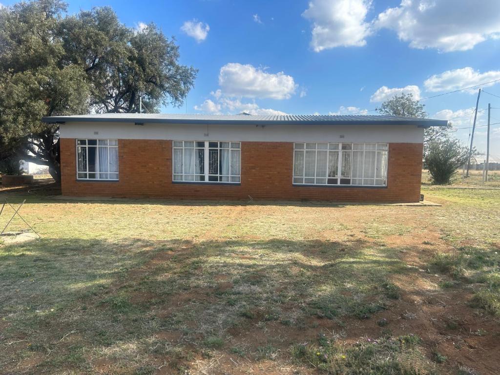 Una pequeña casa de ladrillo con ventanas blancas en un campo. en The Cargo Club Guesthouse, en Ventersburg