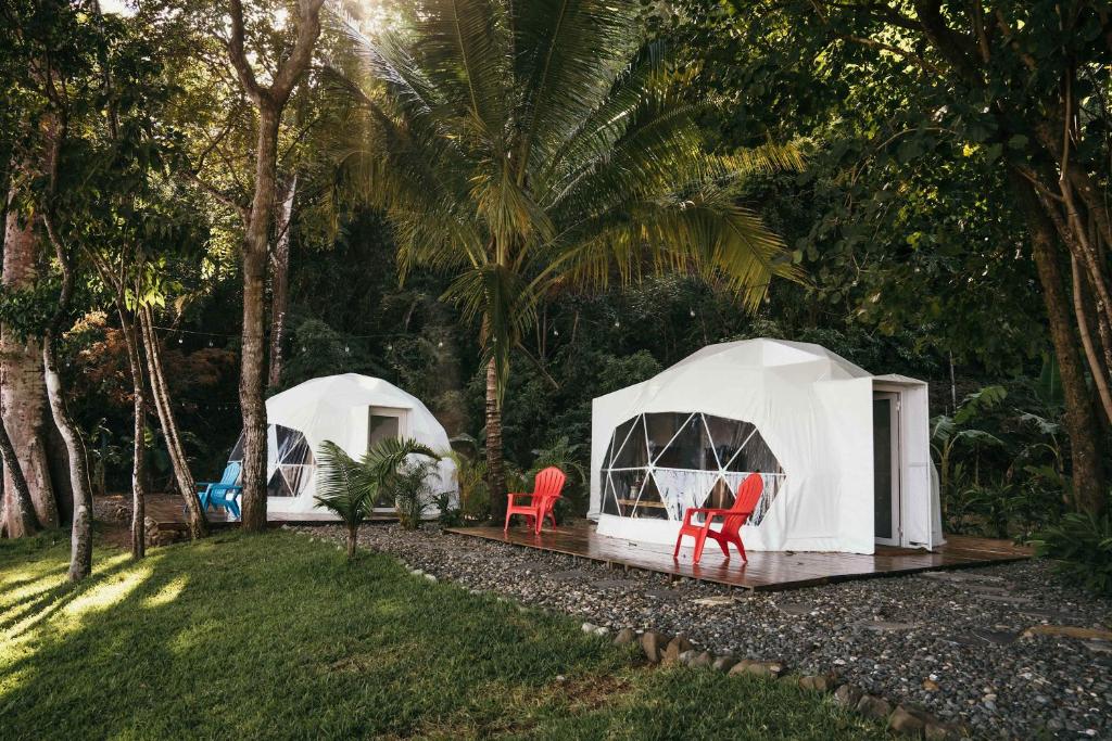 deux tentes blanches dans une cour avec deux chaises rouges dans l'établissement Private Oceanfront Retreat with Jungle Domes, à Playa Venao