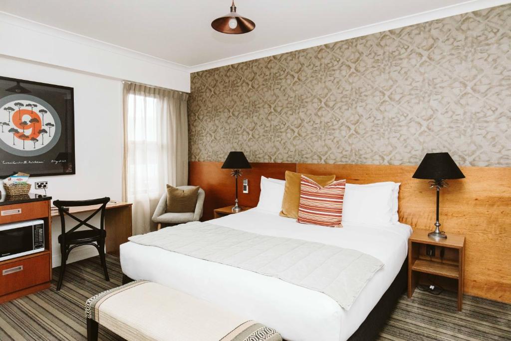 Una habitación de hotel con una cama grande y una silla. en The State Hotel, en New Plymouth