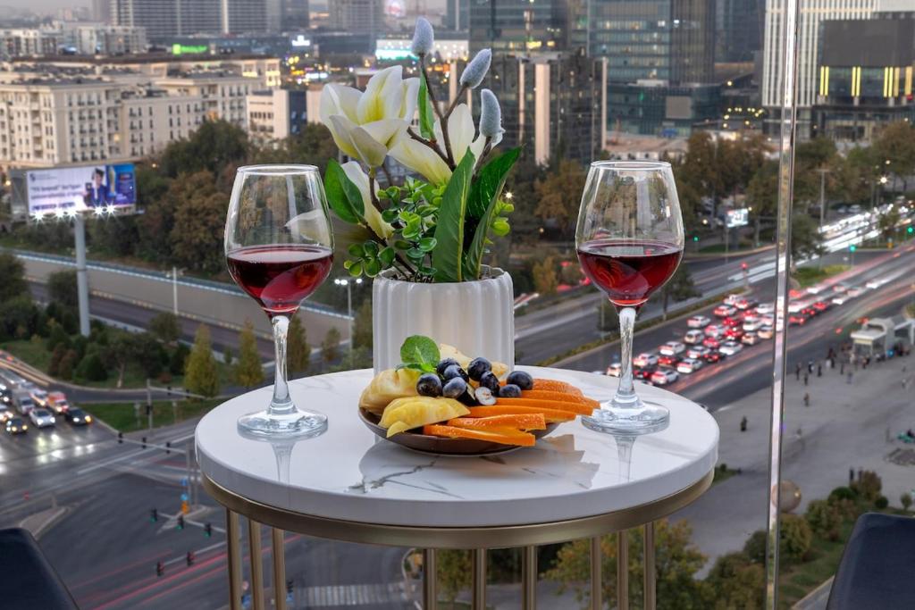two glasses of wine and a plate of food on a table at Urban Luxe U-Tower Tashkent City View Apartment in Tashkent