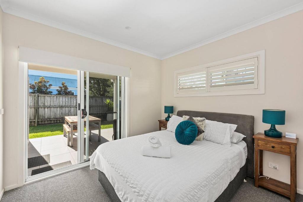 a white bedroom with a bed and a balcony at Sunny Townhouse in Huskisson