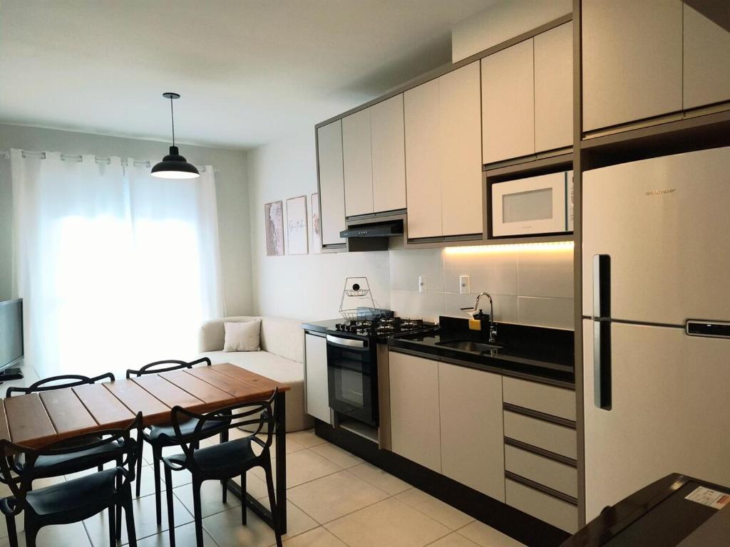 a kitchen with a table and a kitchen with white cabinets at Apartamento novo, 2 quartos a 50 metros da praia in Palhoça