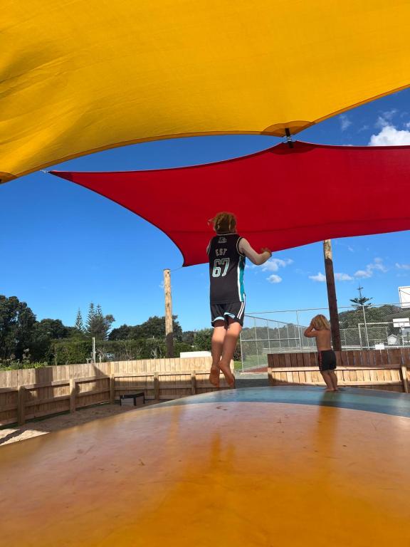 Una persona parada bajo un paraguas rojo y amarillo. en Waipu Cove Surf Cabin, en Waipu
