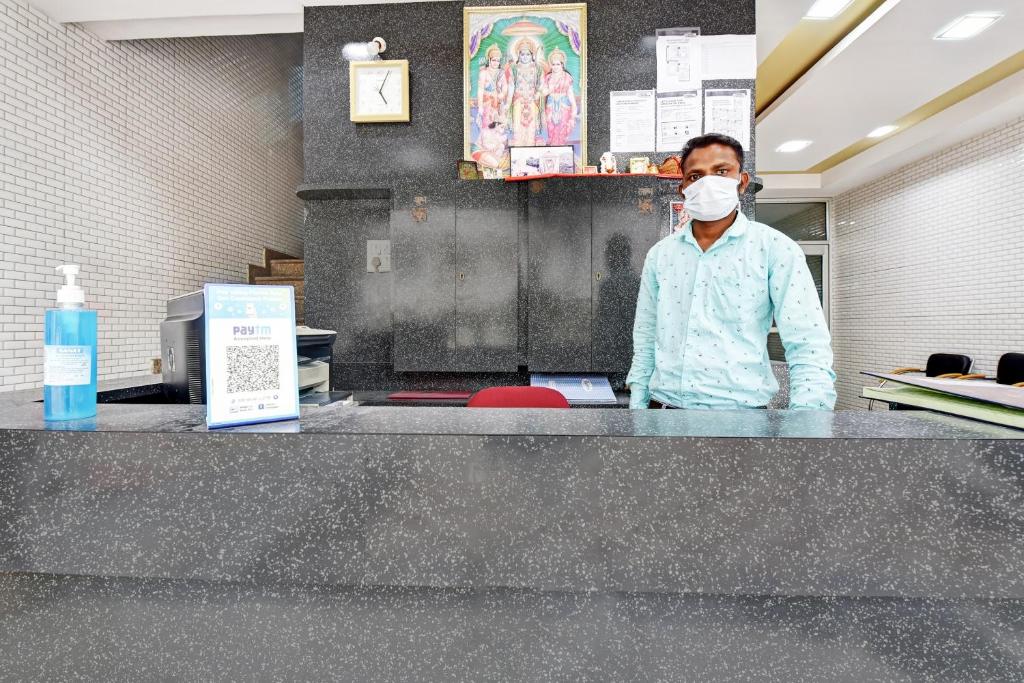 Ein Mann mit einer Gesichtsmaske, der hinter einem Tresen steht. in der Unterkunft Hotel O Eleven Hotel & Banquet in Kota