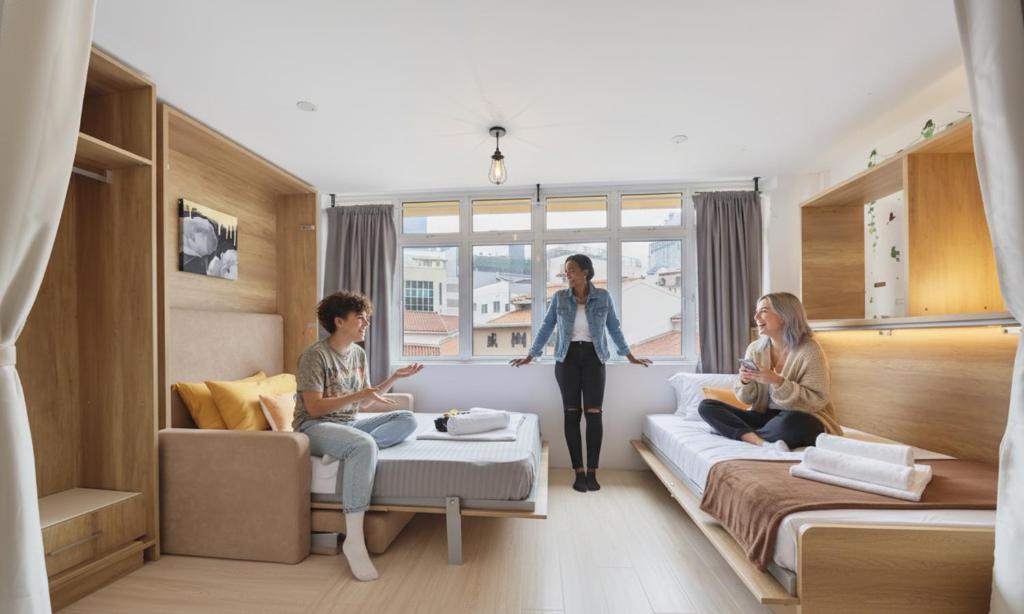 Una mujer parada en una sala de estar con tres personas. en hipstercity hostel, en Singapur