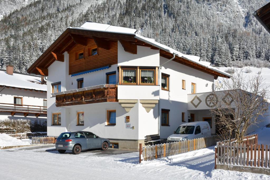una casa en la nieve con dos coches aparcados delante en Haus Schimpfössel en Flirsch