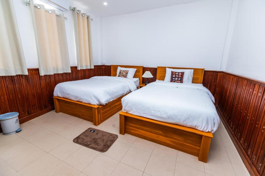 two twin beds in a room with wooden walls at Nisa hostel in Pakse