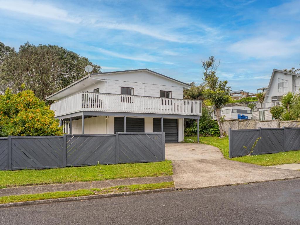 a white house with a balcony on a street at Onemana Magic - Onemana Holiday Home in Opoutere