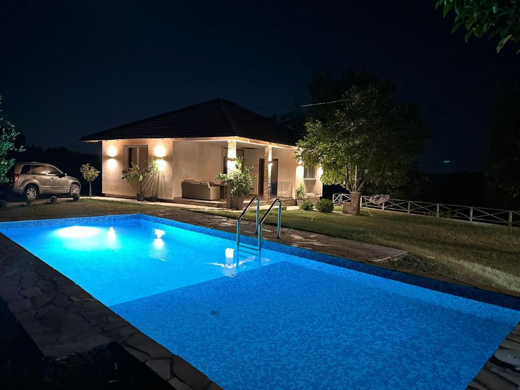 a blue swimming pool in front of a house at night at Slatinska idila - kuća sa bazenom in Bunar
