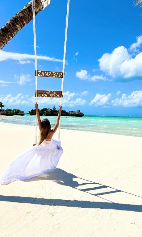 a woman sitting on a swing on the beach at Karibu Beach Resort - Adults Only in Pongwe