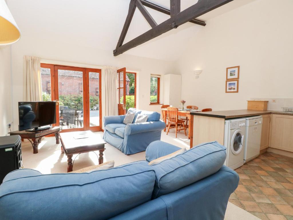 Una sala de estar con un sofá azul y una cocina. en Holly Berry, en Wood Norton