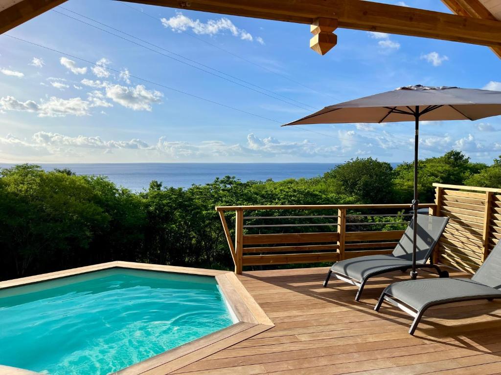a swimming pool on a deck with two chairs and an umbrella at Caribbean Shelter in Bouillante