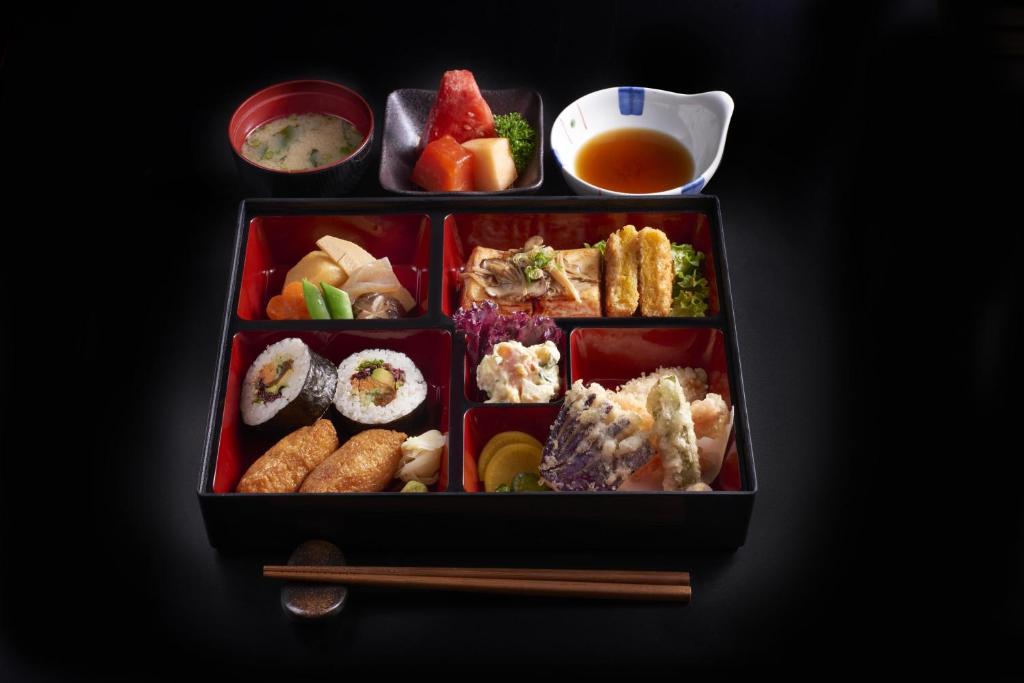 A styled bento meal presented with soup, dipping sauce, sushi, fried items and chopsticks.