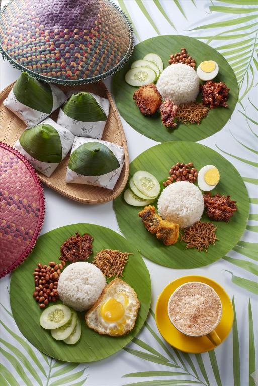 A colourful spread of nasi lemak-style plates, wrapped rice parcels and a hot drink.