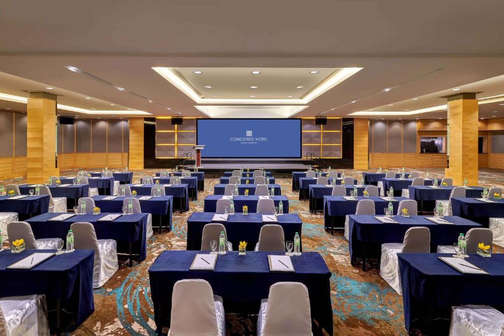 A large ballroom is set for a formal presentation with rows of blue-clothed tables.