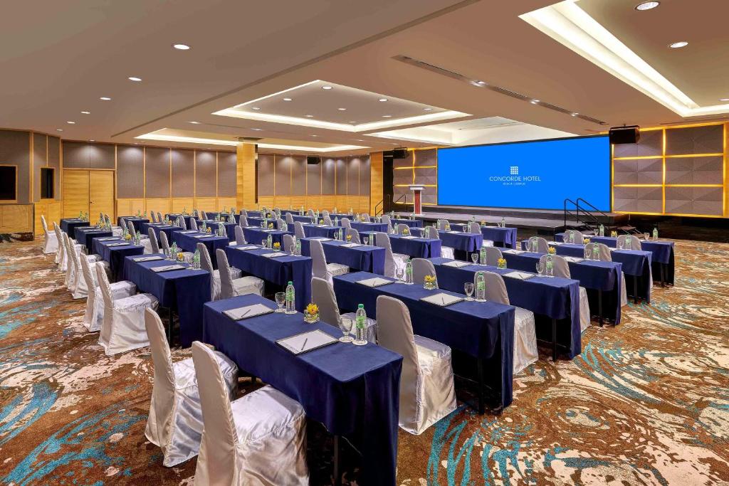 A spacious ballroom is arranged in classroom rows facing a large blue presentation screen.