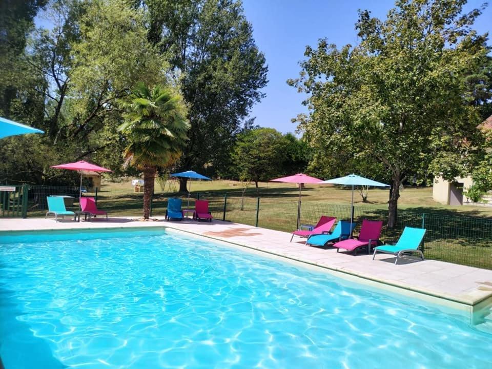 a swimming pool with chairs and umbrellas at Gîte romantique avec bain à remous privatif près de Sarlat in Saint-Cyprien