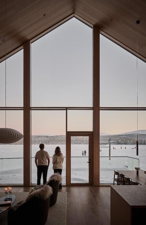 two people standing in a room with large windows at Joiku Luxury Lakeview Chalet in Kolari
