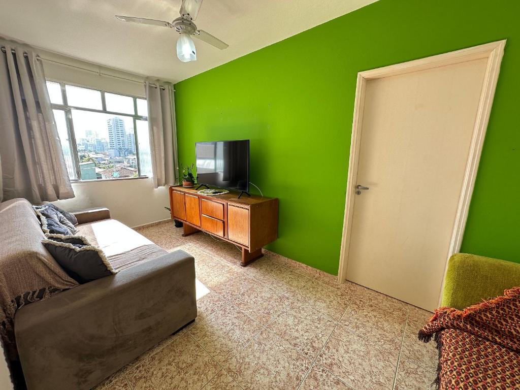 a green living room with a couch and a television at Canto do Forte: conforto, Wi-Fi e garagem! in Praia Grande