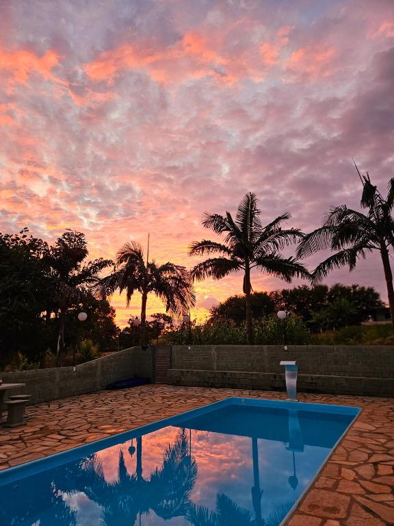 a blue swimming pool with a sunset in the background at Refúgio GRUPOS com piscina, churrasqueiras 38 min Águas Claras Brasília in Brasília