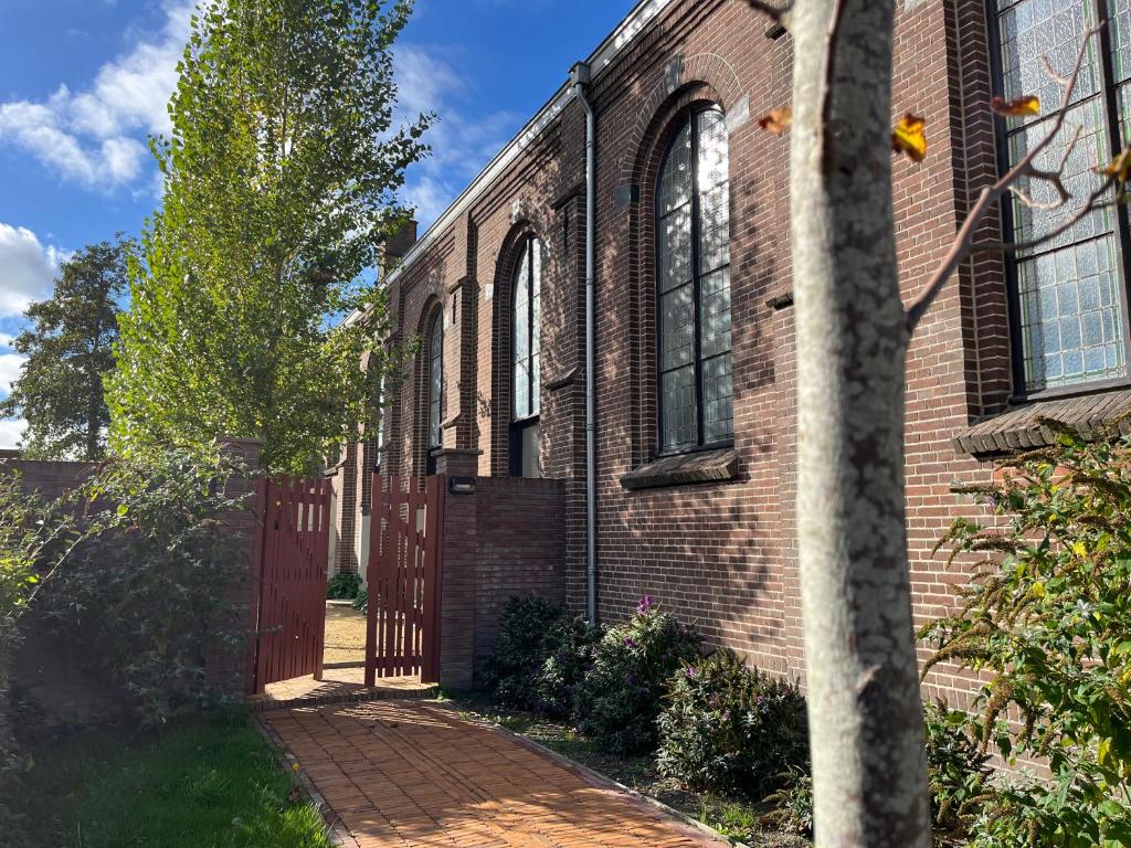 a brick building with a red door and a tree at De Hoffstee in Minnertsga