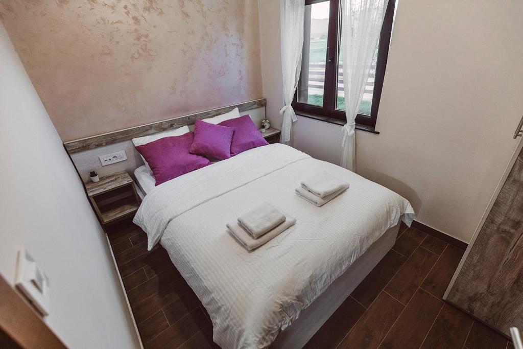 a small bedroom with a bed with purple pillows at Lane Apartmani - Terasa in Vrhpolje