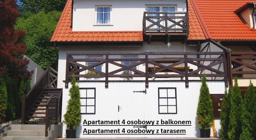 a white building with an orange roof and a staircase at Apartamenty i pokoje Mikołajki in Mikołajki