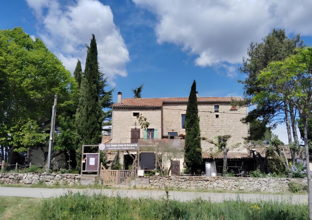 una casa antigua con una pared de piedra y árboles en Gîte Des Louveteaux, en Berrias Et Casteljau