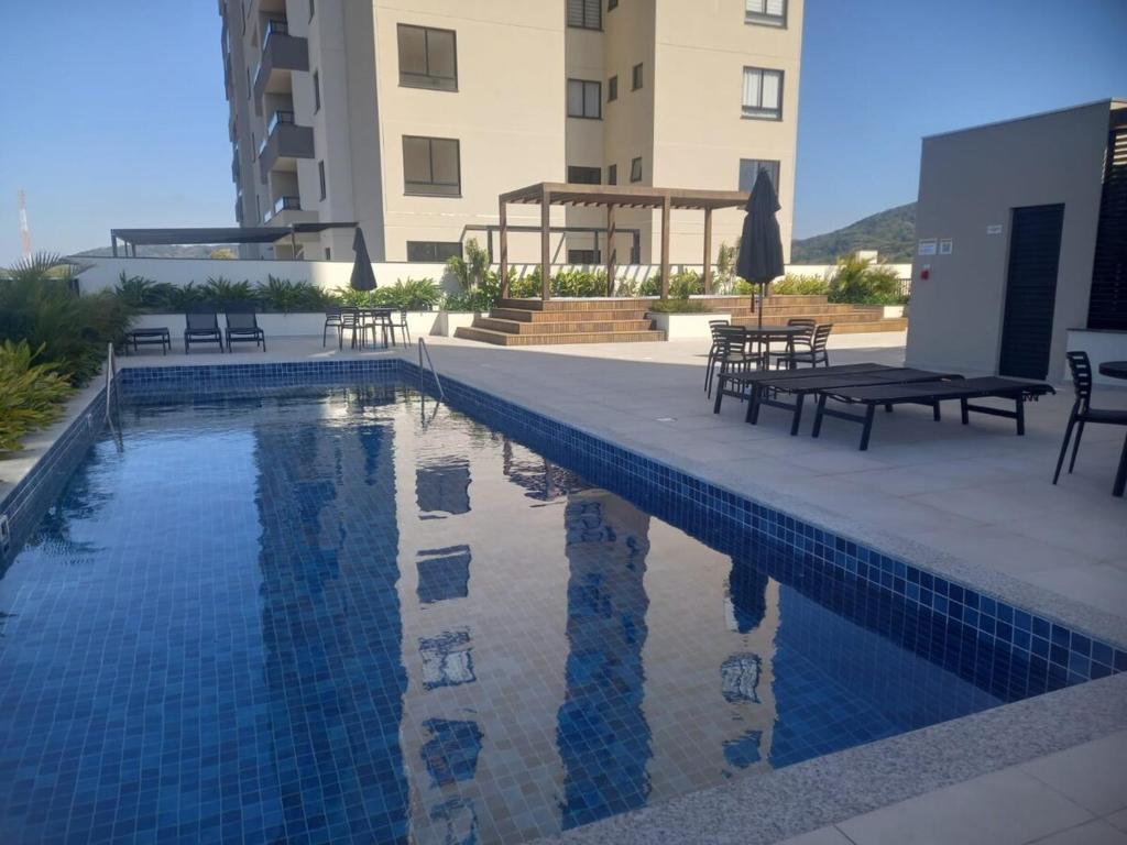 Una piscina con mesas y sillas al lado de un edificio. en Apto com piscina a 150m da Praia!, en Penha